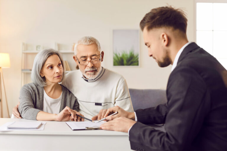A mature expat couple reviewing documents with a real estate agent to buy property in Thailand.